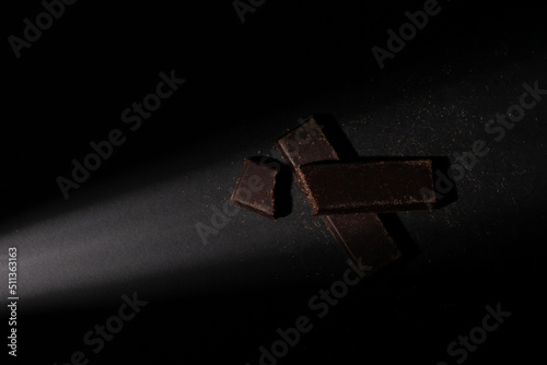 Fototapeta Naklejka Na Ścianę i Meble -  Pieces of chocolate bar illuminated with a soft point light, with an overhead view, on a black background