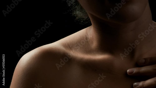 Big close-up shot of fit African American female model with black curly hair strokes her clavicle on black background | Anti-aging concept photo