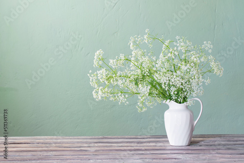 white wild flowers in jug on background green wall photo