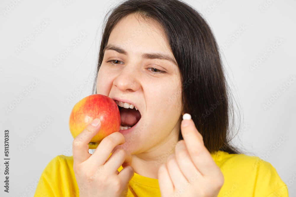 A woman bites a red apple while holding a multivitamin pill in her hand A woman bites a red apple while holding a multivitamin pill in her hand