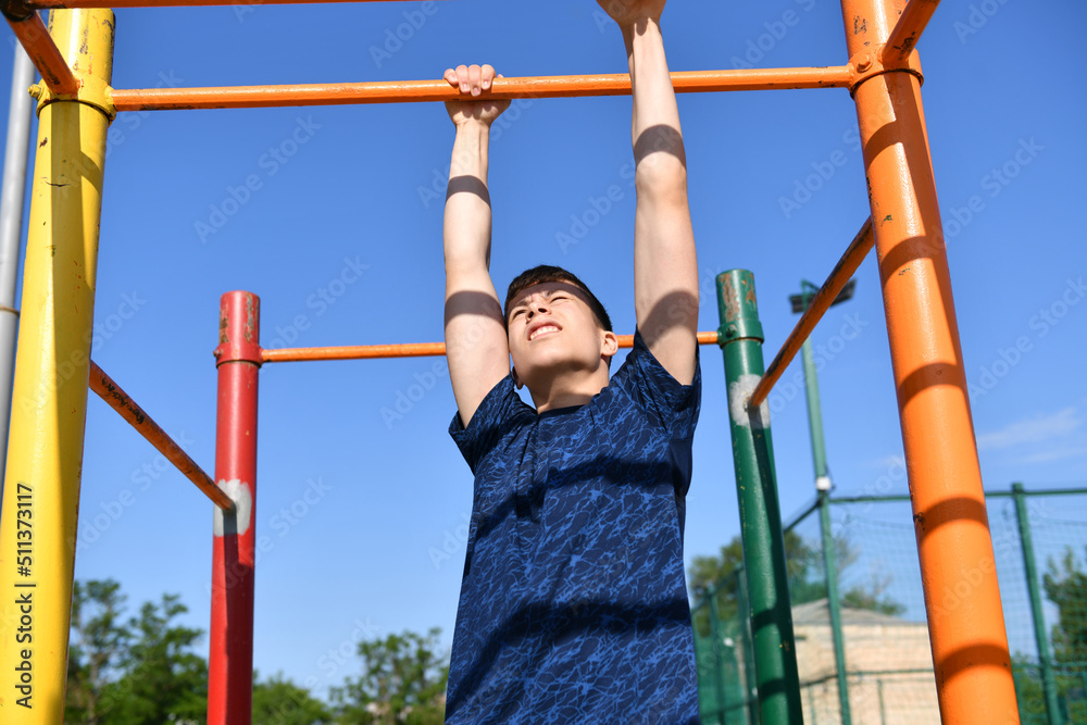 Fototapeta premium a teenage boy trains on a sports ground outdoors, he does physical exercises, a healthy lifestyle, a bright sunny day in summer