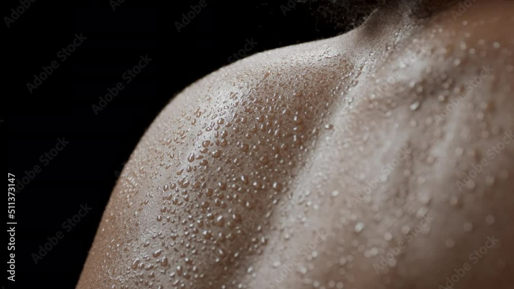 Big close-up shot of young good-looking slim African American female model with dark curly hair moves her wet shoulders on black background | Clean body concept Big close-up shot of young good-looking slim African American female model with dark curly hair moves her wet shoulders on black background | Clean body concept