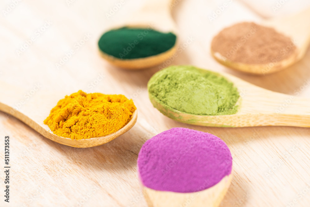 Multicolored superfood powders in spoons: sweet potato, matcha, spirulina, hemp, turmeric, carob on a wooden board. Multicolored superfood powders in spoons: sweet potato, matcha, spirulina, hemp, turmeric, carob on a wooden board.