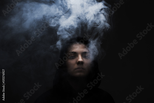 Dark portrait of a short haired girl wearing hoodie with smoke coming out of it. . © Nikola Spasenoski