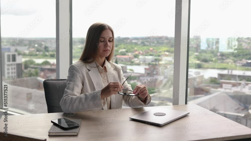 Smiling business woman puts on glasses, opens her laptop and sits at her desk. Happy office worker, business woman working on a laptop at the table from the office. Starting the day at the office Smiling business woman puts on glasses, opens her laptop and sits at her desk. Happy office worker, business woman working on a laptop at the table from the office. Starting the day at the office