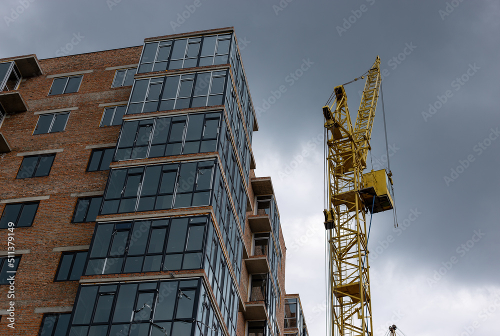 Fototapeta premium Yellow tower crane against dramatic sky — urban development and industry background