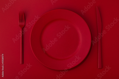 Red plate with the red cutlery on the red background.