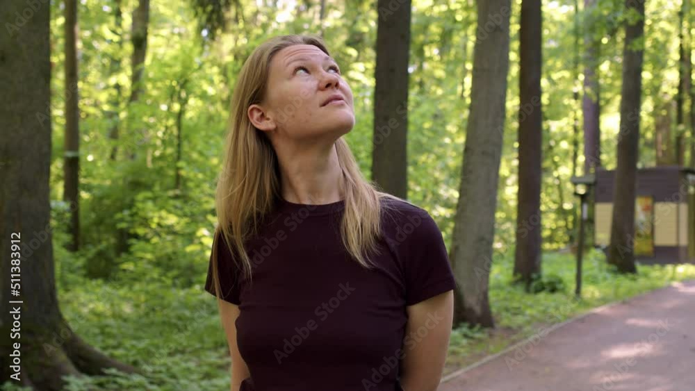 beautiful slender blonde walks through picturesque green forest at sunset or dawn. woman in black t-shirt looks up at birds or treetops. lady on walk in forest walks alone along paths. beautiful slender blonde walks through picturesque green forest at sunset or dawn. woman in black t-shirt looks up at birds or treetops. lady on walk in forest walks alone along paths.