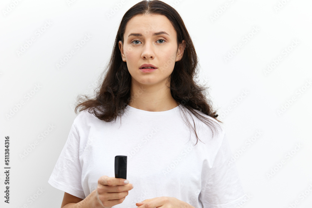 a sweet, pretty woman with long dark hair stands on a white background in a white T-shirt and holds a black comb in her hands, looking pleasantly at the camera a sweet, pretty woman with long dark hair stands on a white background in a white T-shirt and holds a black comb in her hands, looking pleasantly at the camera