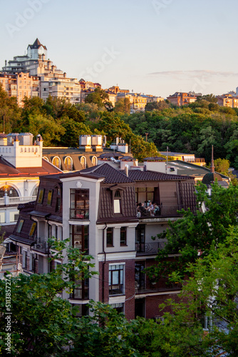 Urban hill with trees and buildings rooftops under sunset sky