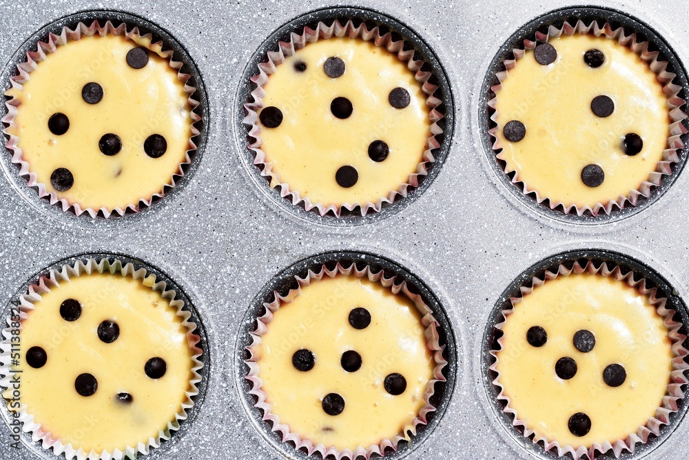Fototapeta premium Baking tray with muffins paper cases filled with muffin dough, ready for baking. Making of muffins with chocolate chips