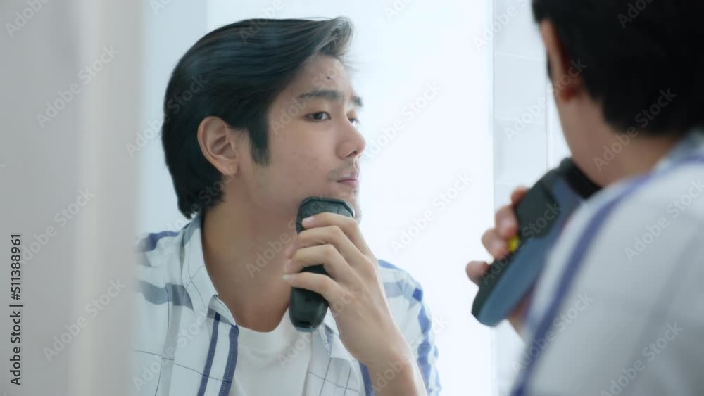 Health concept of 4k Resolution. Young Asian man shaving in the bathroom. look in the mirror. electric shaver. Health concept of 4k Resolution. Young Asian man shaving in the bathroom. look in the mirror. electric shaver.