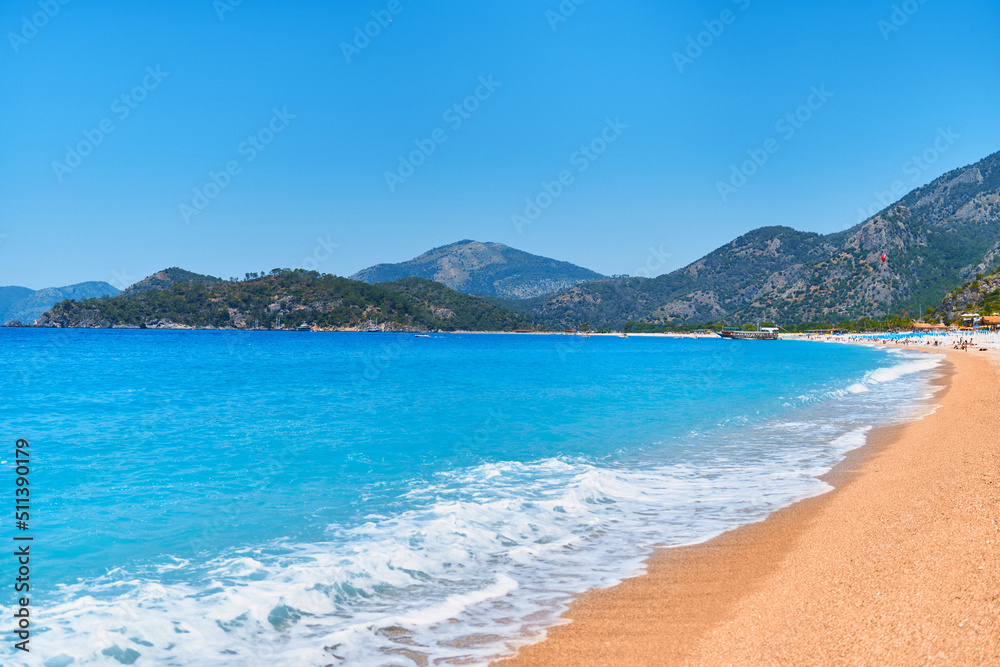 Background of turquoise sea, blue clear sky, sandy beach and mountains in a sunny summer day