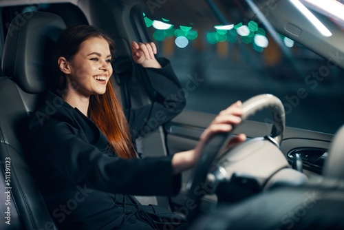 a happy, relaxed woman enjoys a night ride at the wheel while sitting in a car and smiling broadly squints her eyes with happiness © SHOTPRIME STUDIO