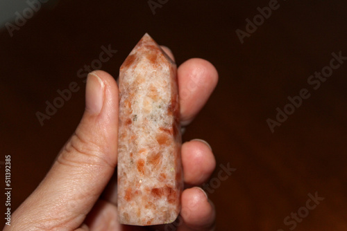 Person holding a polished sunstone point also known as a sunstone tower crystal. Sunstone is a healing stone that works across the physical, spiritual, and emotional plains. (heliolite) gem stone photo