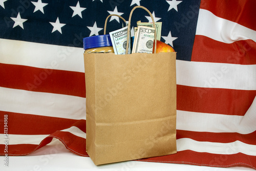 A plain brown paper bag filled with groceries and money on an American flag  