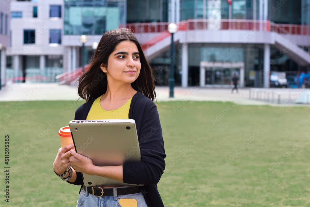 Obraz premium Young girl student walking on campus with laptop computer and coffee cup