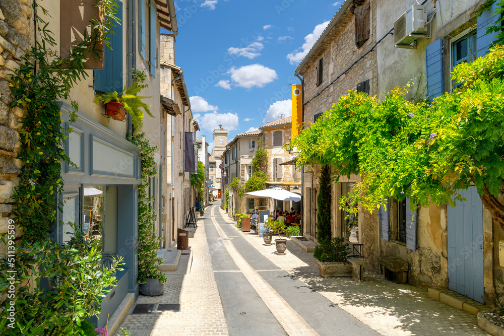 Fototapeta premium A picturesque street through the historic town of Saint-Remy de Provence, France, with the colorful shops and cafes and the clock tower in view on a summer day.