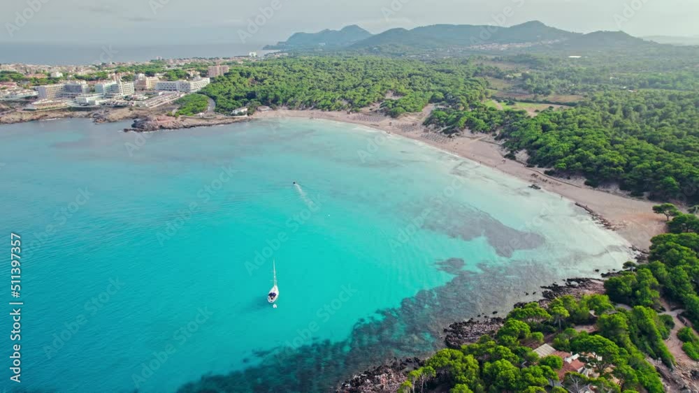 Top view of umbrellas by the beach with turquoise waters and tropical coastline. People relaxing by sandy Cala Agulla Beach with the crystal clear blue water on Majorca, Balearic Islands, Spain. Top view of umbrellas by the beach with turquoise waters and tropical coastline. People relaxing by sandy Cala Agulla Beach with the crystal clear blue water on Majorca, Balearic Islands, Spain.