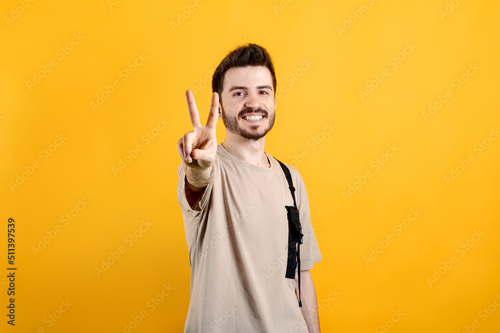 Cheerful young man wearing t-shirt posing isolated over yellow background showing and pointing up with fingers number two while smiling.