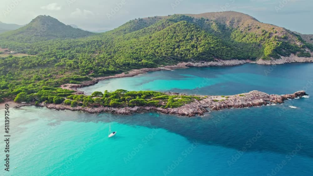 Vessel sailing by a Beautiful tropical green rocky coast with turquoise waters. Paradise alike bay in Cala Agulla, Mallorca, Balearic Islands, Spain with a tourist boat exploring the location.