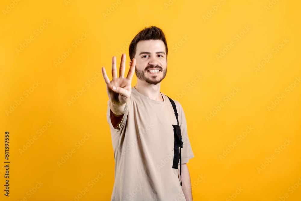 Cheerful young man wearing t-shirt posing isolated over yellow background showing and pointing up with fingers number four while smiling. Cheerful young man wearing t-shirt posing isolated over yellow background showing and pointing up with fingers number four while smiling.