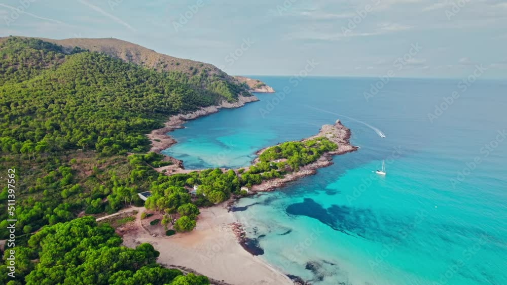 Vessel sailing by a Beautiful tropical green rocky coast with turquoise waters. Paradise alike bay in Cala Agulla, Mallorca, Balearic Islands, Spain with a tourist boat exploring the location. Vessel sailing by a Beautiful tropical green rocky coast with turquoise waters. Paradise alike bay in Cala Agulla, Mallorca, Balearic Islands, Spain with a tourist boat exploring the location.