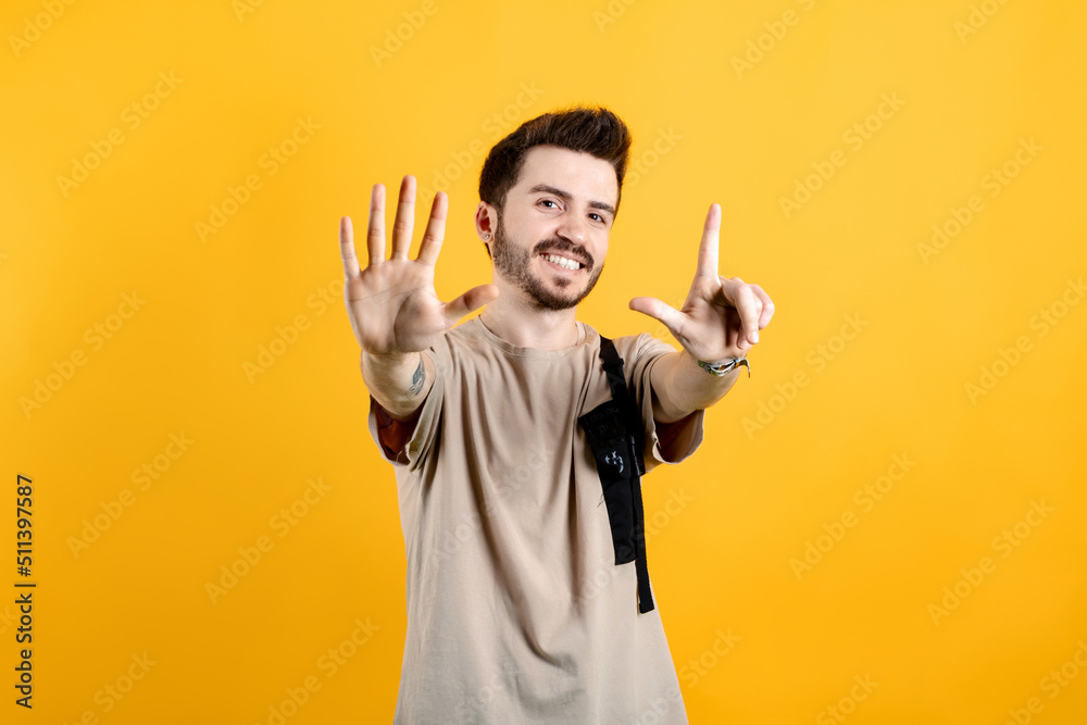 Happy young man wearing beige t-shirt posing isolated over yellow background showing and pointing up with fingers number seven while smiling. Happy young man wearing beige t-shirt posing isolated over yellow background showing and pointing up with fingers number seven while smiling.