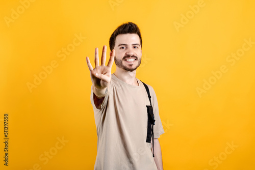 Cheerful young man wearing t-shirt posing isolated over yellow background showing and pointing up with fingers number four while smiling.