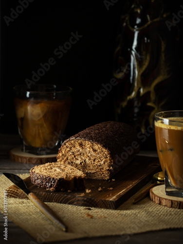 Chocolate cake roll with cut piece on wooden board and coffee. Rustic style with copy space