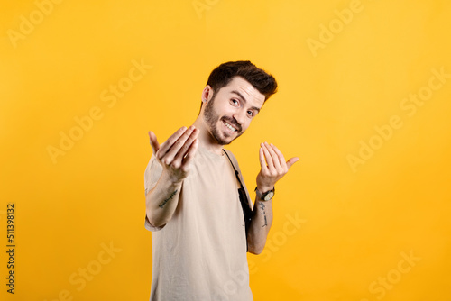 Handsome young man wearing casual clothes posing isolated over yellow background inviting to come closer with hands. Happy that you came. photo