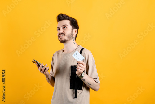 Caucasian young man wearing t-shirt posing isolated over yellow background buying with the mobile with a credit card while thinking. Online shopping concepts. © platinumArt