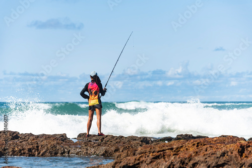 Fisherman woman with fishing rod on the rocks fishing photo