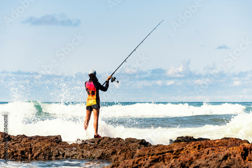 Fisherman woman with fishing rod on the rocks fishing photo