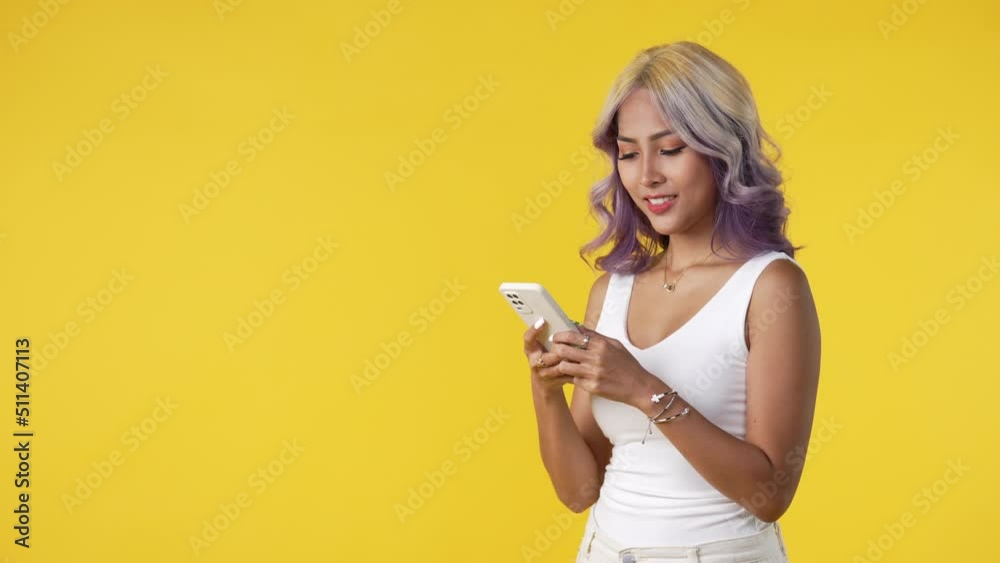 Happy and cheerful young Asian woman using smartphone isolated on yellow background Happy and cheerful young Asian woman using smartphone isolated on yellow background