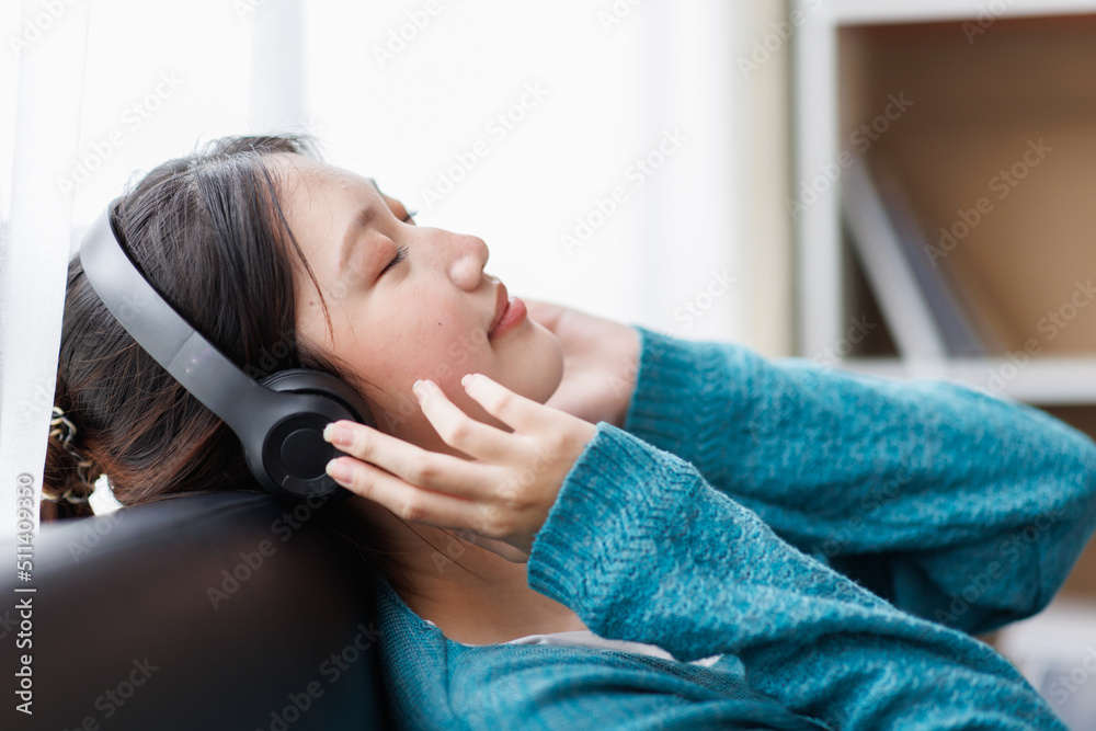 Young Asian woman with headphones relaxing at home late at night, she is lying on the armchair and listening to music using a tablet Young Asian woman with headphones relaxing at home late at night, she is lying on the armchair and listening to music using a tablet