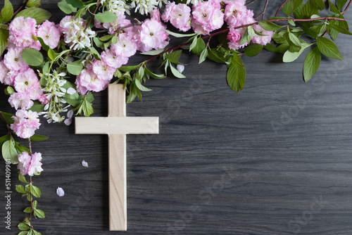 Wood cross with border of branches with pink and white flower blossoms on a dark wood background with copy space