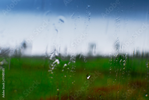 Abstract image of monsoon, blurred blue sky with green natural foreground and raindrops on glass creating rainy mood. Rainy season or monsoon season of rural India.