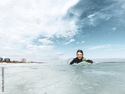 Young boy paddling surfboard in ocean looking at camera with high rise buildings in background
