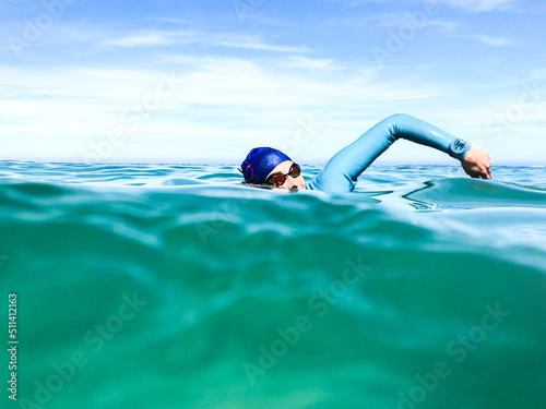 Swimmers upper body seen from water level doing freestyle stroke wearing wetsuit, cap and goggles