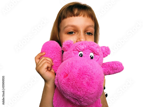 A cute Caucasian girl of 7 years old with blond hair cuddles and hugs a pink hippopotamus. Hippo plush toy. An expression of love, affection, favor. Game in daughters - mothers. Childhood adolescence. photo