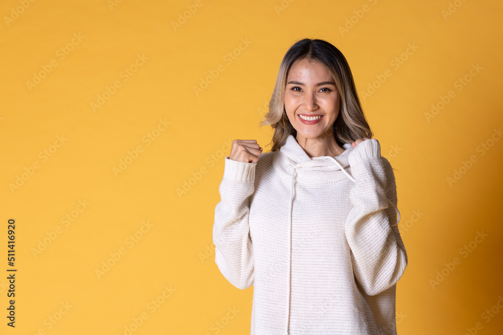 A young Asia woman with long hair in a knitted sweater color white facial expression and use sign language for communication on yellow background. A young Asia woman with long hair in a knitted sweater color white facial expression and use sign language for communication on yellow background.