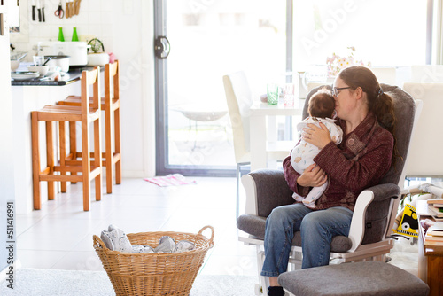 Young mum in fourth trimester singing newborn baby to sleep on rocking chair in messy house
