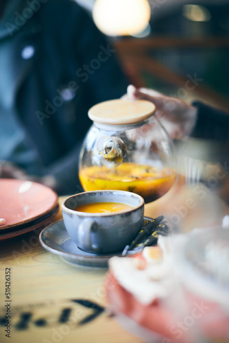 A woman pours sea buckthorn tea from a teapot into a mug. Vertical photo.