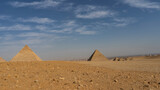 The great pyramids of Chephren, Mykerinus and the small pyramids of queens against the blue sky. Stones on the yellow sand of the Giza plateau. The houses of Cairo are visible in the distance. Egypt