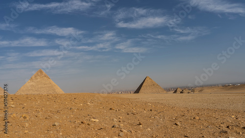 The great pyramids of Chephren  Mykerinus and the small pyramids of queens against the blue sky. Stones on the yellow sand of the Giza plateau. The houses of Cairo are visible in the distance. Egypt
