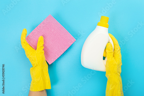 The hands of a housewife in yellow rubber protective gloves hold a bottle of household chemicals and a rag. Detergent for various surfaces in the kitchen, bathroom and other rooms. 