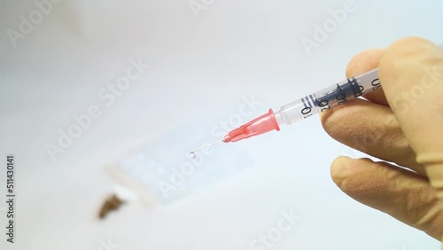In a hand in a medical glove, a syringe on a needle, a drop of medicine