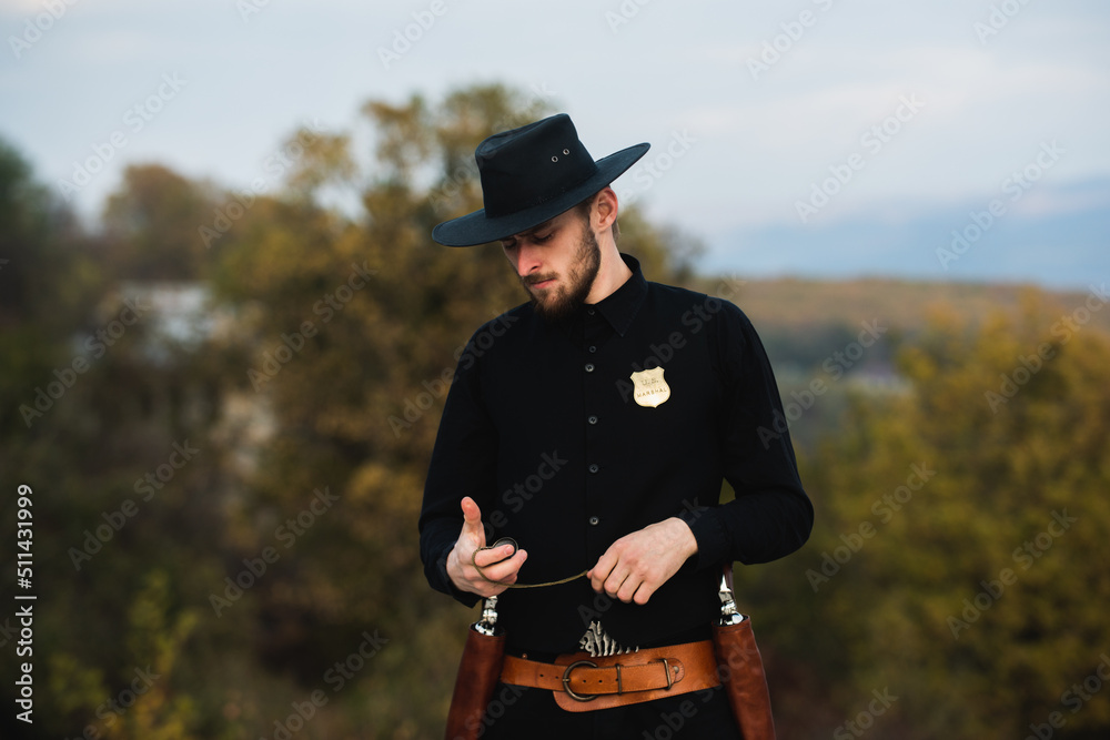 Fototapeta premium Sheriff or cowboy in black suit. Man with vintage pistol revolver and marshal ammunition. American western Sheriff. Wild west with cowboy.