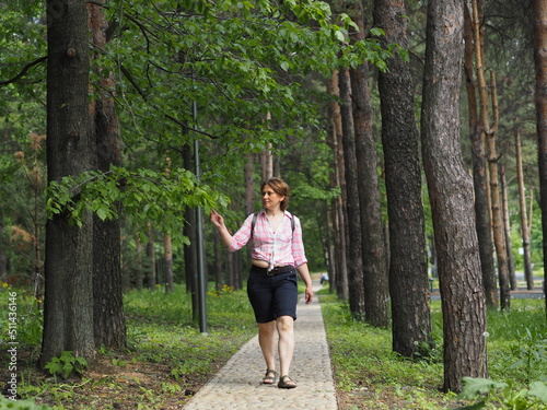 A woman walks in the summer in the park in sunny weather, she walks along a forest path.